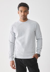 Grijze sweatshirt met een ronde hals, geribbelde manchetten en onderrand, met een gladde textuur en raglanmouwen. Gecombineerd met zwarte broek.