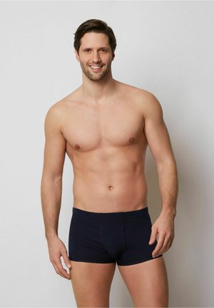 Boxers en coton bleu marine avec une coupe ajustée, taille élastique et sans motifs ni logos visibles. Le modèle se tient avec une expression neutre.