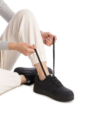 Zapatillas negras con cordones hechas de material suave, con una suela gruesa, parte superior perforada y acentos de logo en contraste.