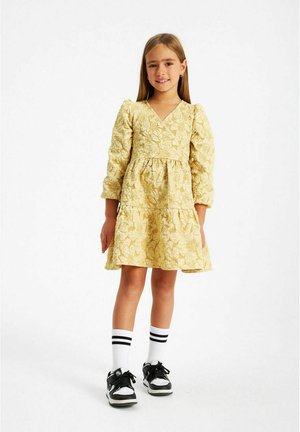 Vestito giallo con motivo floreale, maniche lunghe a sbuffo, scollatura a V e gonna svasata, abbinato a sneakers nere e calzini bianchi a righe.