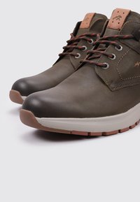 Zapatos de cuero marrón con un acabado suave, suela de goma clara en contraste y cordones oscuros. Presentan un acento de cuero color marrón claro en la lengüeta.