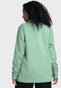 Green corduroy shirt with long sleeves and buttoned cuffs, featuring a textured ribbed pattern, slightly oversized fit, and a straight hem.