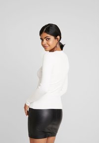Haut à manches longues blanc côtelé associé à une mini-jupe en cuir noir. Le haut présente un design ajusté et un col rond.