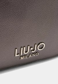 Brunet tekstureret læderoverflade med et guldfarvet præget logo "LIU·JO MILANO" med afrundede detaljer.