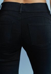 Schwarze Denim-Jeans mit einem mittelhohen Bund, ausgestattet mit zwei Gesäßtaschen und einem glatten, strukturierten Stoff. Die Nähte sind dezent und passen zur Farbe.