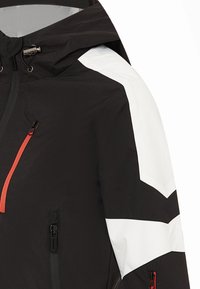 Giacca bianca e nera con cappuccio, tasche con cerniera e una cerniera arancione come accentuazione. Il design include forme geometriche e tessuto testurizzato.
