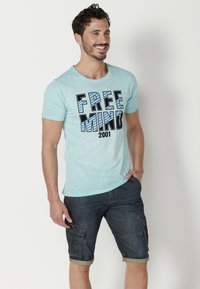Világoskék pamut póló "FREE MIND 2001" grafika fekete és kék színekben, sötét farmer cargo sorttal párosítva, felgöngyölt szegélyekkel.
