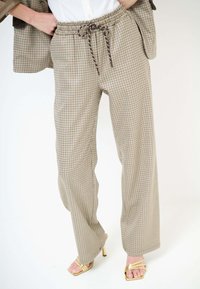 Pantaloni beige a quadri a gamba larga con vita elastica e coulisse, indossati con blazer coordinato e sandali dorati con tacco alto e cinturini.