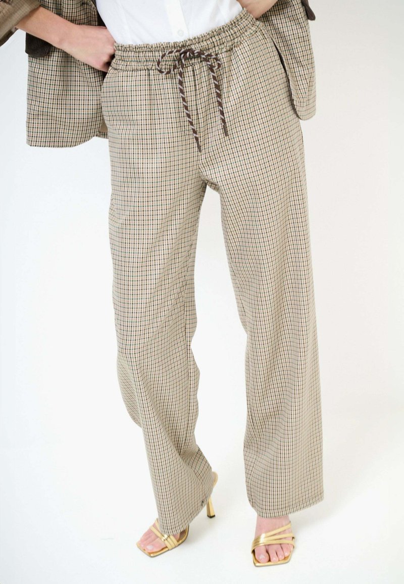 Pantaloni beige a quadri a gamba larga con vita elastica e coulisse, indossati con blazer coordinato e sandali dorati con tacco alto e cinturini.