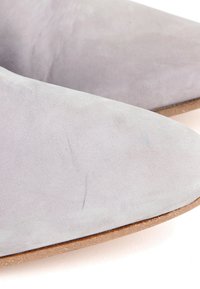 Gros plan de l’avant et du côté d’une chaussure en suède gris clair avec une semelle marron sur fond blanc.