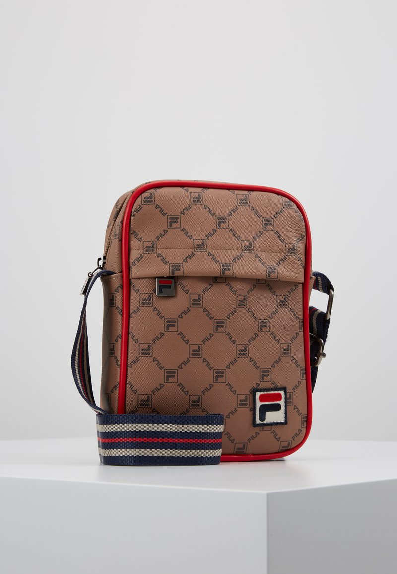 Sac synthétique marron avec un motif de logo répétitif, garniture rouge et une bandoulière ajustable rayée. Il dispose d'une poche avant avec un détail de logo.