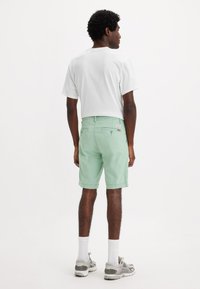 Shorts verde menta con elastico in vita e tasche posteriori, abbinati a una camicia bianca. Il modello indossa calze bianche e sneakers grigie.