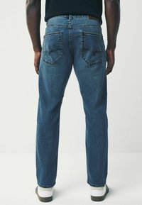 Jean en denim de lavage moyen, design à jambe droite. Dispose de deux poches arrière et de détails de couture subtils. Associé à des baskets blanches.