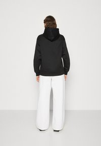 Felpa nera con cappuccio, dal fit rilassato e polsini a coste, abbinata a pantaloni bianchi a gamba larga, con texture liscia e design minimalista.