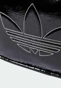 Borsa in vernice nera con un logo in rilievo prominente che presenta tre foglie e strisce orizzontali, delineato da cuciture bianche.