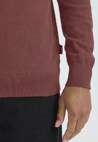 Bordó kötött pulóver hosszú ujjakkal és bordás mandzsettákkal. Oldalsó hasítékkal és egy kis címkével a szegény. Puha tapintású.