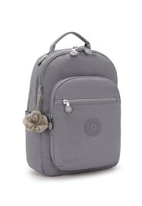 Sac à dos en nylon gris à la forme arrondie, avec deux compartiments zippés, une poche avant et un logo circulaire. Il est doté d'un accessoire de porte-clés en forme de singe en peluche.