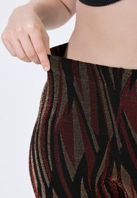 Leggings a vita alta neri con motivi a zigzag metallici rossi e dorati. Tessuto a maglia elasticizzato con una texture liscia e cintura elastica.