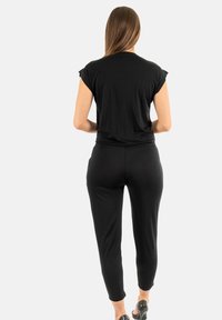 Set lounge nero composto da una maglietta a maniche corte e pantaloni taper. Tessuto morbido, vestibilità rilassata, design semplice senza pattern visibili.