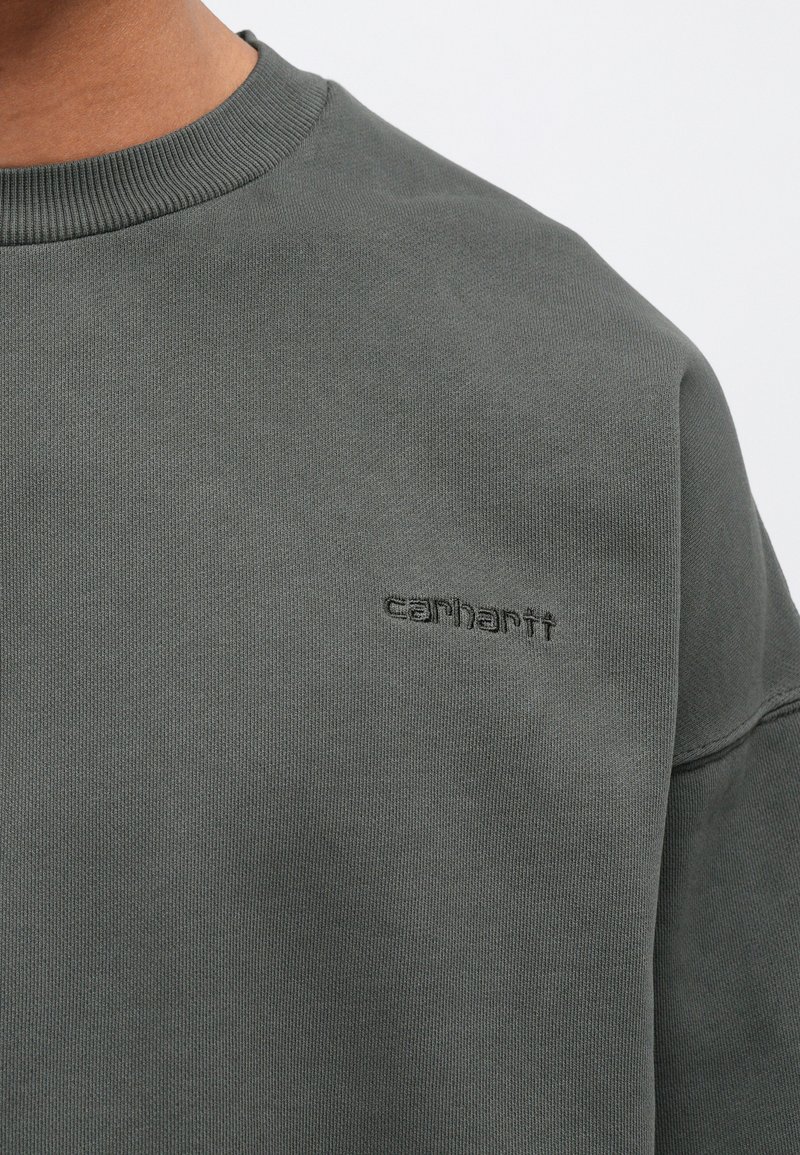 Sudadera verde oscuro con cuello de canalé, que presenta un discreto logotipo bordado de "carhartt" en el pecho, hecha de tela texturizada.