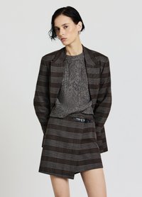 Braun-grauer Kariertblazer mit breiten Revers, kombiniert mit einem strukturierten, grauen Strickpullover und einem passenden kurzen Rock mit Gürtel.