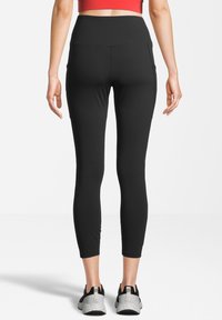 Czarne legginsy sportowe z wysokim stanem, wyposażone w boczne kieszenie oraz gładką, elastyczną fakturę. Połączone z czarno-szarymi butami sportowymi.