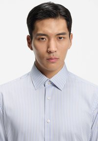 Camicia a righe azzurro chiaro e bianco con colletto appuntito, chiusura con bottoni e tessuto dalla texture liscia.