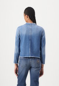 Veste en denim avec un ourlet effiloché et un pantalon en denim assorti, tous deux dans un délavage bleu clair, avec un design de logo discret sur la poche arrière.