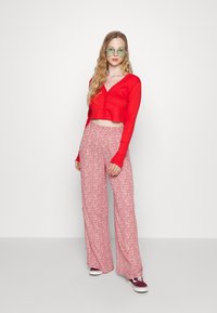 Top cropped vermelho com nervuras, decote em V e detalhe de botões, combinado com calças largas rosa com padrão floral e ténis bordeaux.
