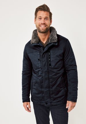 Dark blue jacket with a faux fur collar, featuring zip and button closures, multiple front pockets, and a textured fabric finish.