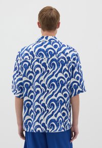 Camisa de manga corta con una tela blanca y un patrón azul en forma de remolino, cuello abotonado y corte relajado. Textura suave y diseño casual.