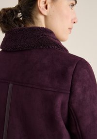 Giacca in suede viola con colletto in pile testurizzato, caratterizzata da una finitura liscia, cuciture dritte e un design minimalista.