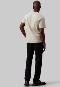 Beige katoenen t-shirt met een losse pasvorm, korte mouwen en een ronde halslijn, gecombineerd met zwarte rechte jeans en zwarte schoenen.