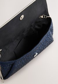 Navy blue clutch purse with textured exterior, opening to a black fabric interior. Features a snap closure and an inner pocket.