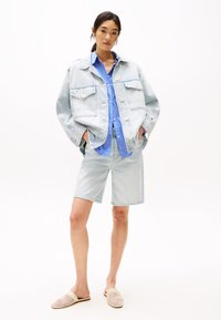 Ljusblå denimjacka med två bröstfickor, i kombination med en blå och vit randig skjorta samt ljusblå shorts. Beige vävda mules.