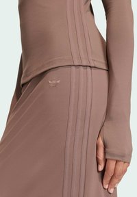 Brown athletic top and skirt with three white stripes and a small embroidered logo. Smooth fabric with a fitted design and thumbholes.