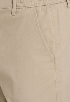 Pantalones de algodón beige con un acabado texturizado, que cuentan con un bolsillo lateral y una cinturilla elástica para mayor comodidad. Primer plano del detalle de la tela.