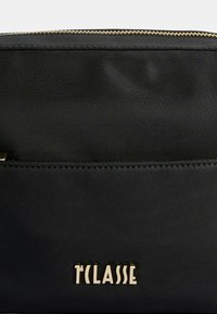 Borsa a pochette nera in nylon con cerniera e logo color oro. Presenta una texture liscia e un design minimalista.