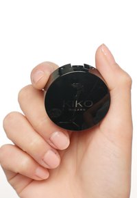 Black compact with KIKO MILANO logo, held in a hand. Smooth texture, round shape, and minimalist design. Fingernails have a light pink polish.