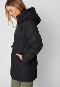 Chaqueta acolchada negra con capucha, con diseño acolchado, bolsillos laterales y cremallera frontal. El material parece suave e insulated.
