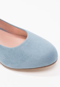 Chaussure plate en daim bleu clair avec bout rond et doublure intérieure beige sur fond blanc.