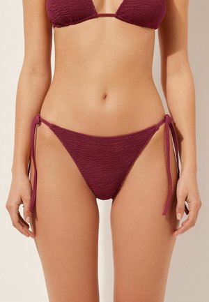 Burgunderfarbener Bikini aus strukturiertem Stoff, mit dreieckigem Oberteil, verstellbaren Bindebändern an den Seiten und minimalem Schnitt am Unterteil.