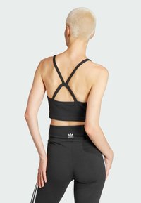 Sujetador deportivo negro recortado con un diseño de espalda nadadora, que presenta una textura suave y un estilo minimalista, combinado con leggings negros de tiro alto.