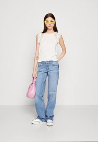 Hvit topp med blonde detaljer, lyseblå jeans, gule solbriller og en rosa veske. Hvite joggesko fullfører det avslappede antrekket.