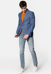 Niebieska kratkowana marynarka, zapięta, noszona na pomarańczowym swetrze; jasnoniebieskie dżinsy; białe trampki z brązowymi akcentami; gładki materiał, nowoczesny krój.