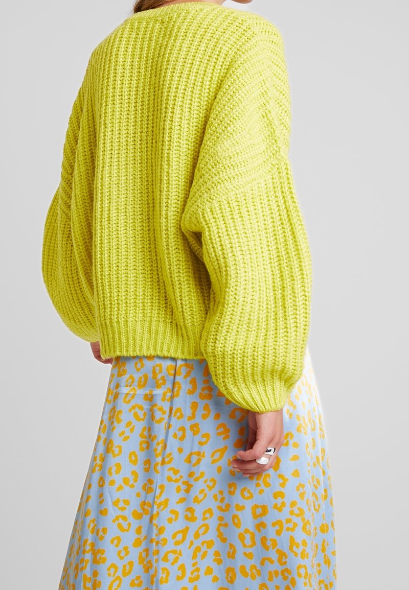 Knitted yellow sweater with a loose fit and oversized sleeves, paired with a blue skirt featuring a yellow leopard print.