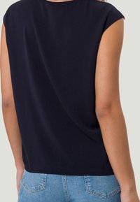 Top blu navy con maniche a cuffia corte, caratterizzato da una texture liscia e una vestibilità comoda, abbinato a jeans di denim blu chiaro.