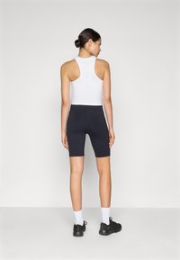 Pantaloni sportivi neri abbinati a un top bianco senza maniche, mostrati da dietro. L'outfit presenta un design aderente e superfici lisce.