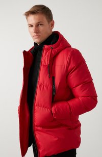 Rød puffjakke med hætte, frontlynlås og sidelommer. Fremstillet af glat materiale med quiltet design og sorte detaljer.