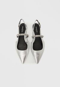 Ασημί μπαλαρίνες με λουράκι πίσω και μυτερή μύτη. Διαθέτουν διακοσμητικό λουράκι με μεταλλική λεπτομέρεια. Ομαλή, γυαλιστερή υφή και μαύρη σόλα.